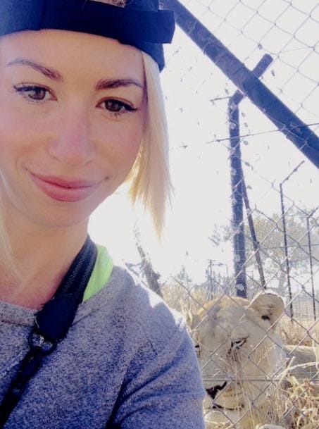 blonde woman taking selfie with lion in background